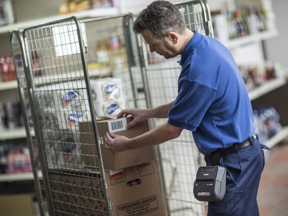 Warehouse worker applying a barcode label onto a brown box, that has been printed on the Brother RJ portable printer